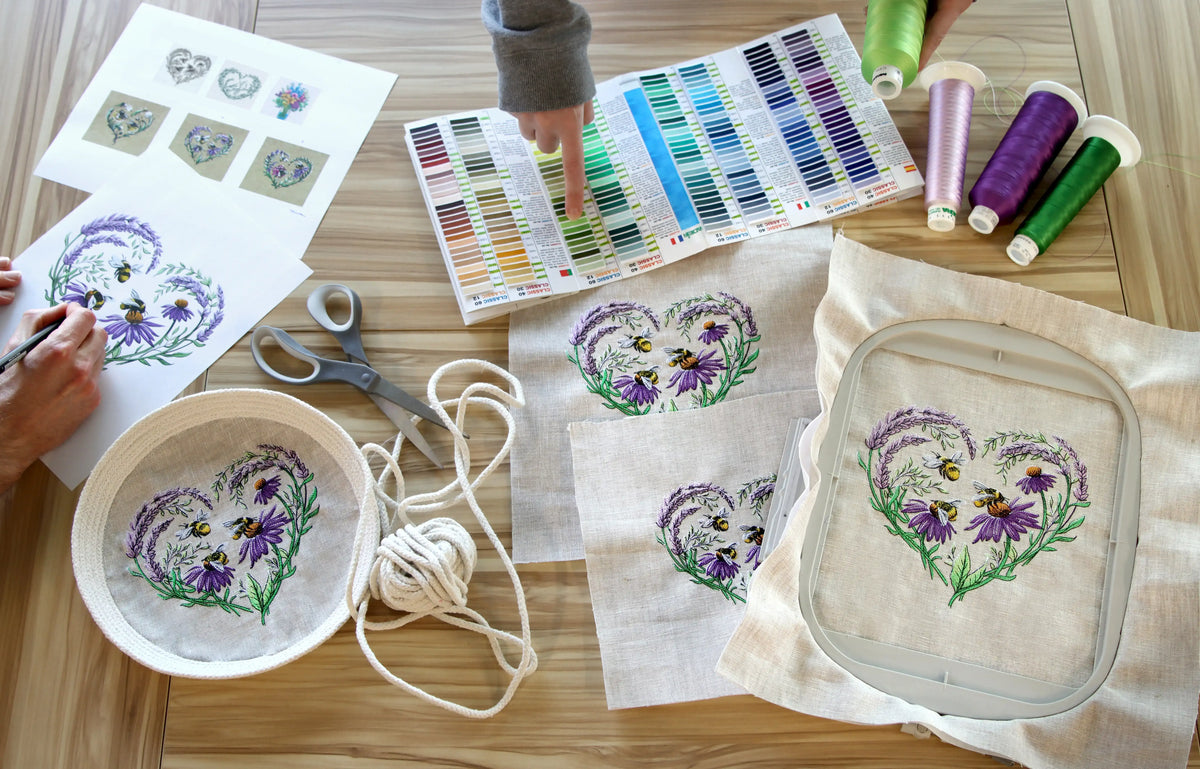 machine embroidery project with heart lavender bee designs, threads, and tools on a wooden table.